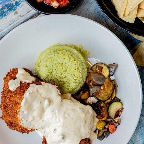 Crispy chicken with creamy sauce, green rice, and roasted vegetables on a white plate.