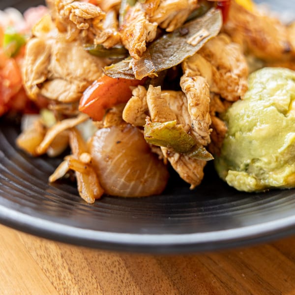 Close-up of Prados Modern Mexican Cantina's chicken fajitas with onions, peppers, and guacamole.
