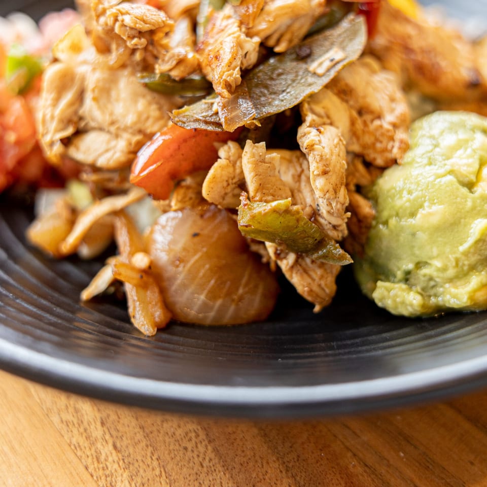 Close-up of Prados Modern Mexican Cantina's chicken fajitas with onions, peppers, and guacamole.