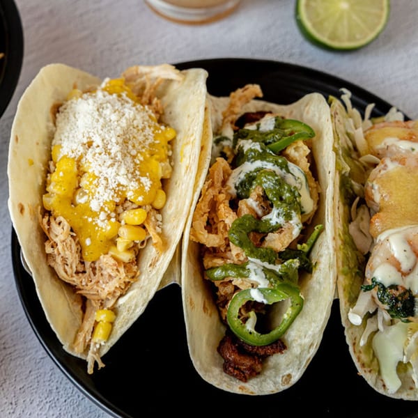 Three Prados Modern Mexican Cantina tacos on a black plate, with various fillings and toppings.