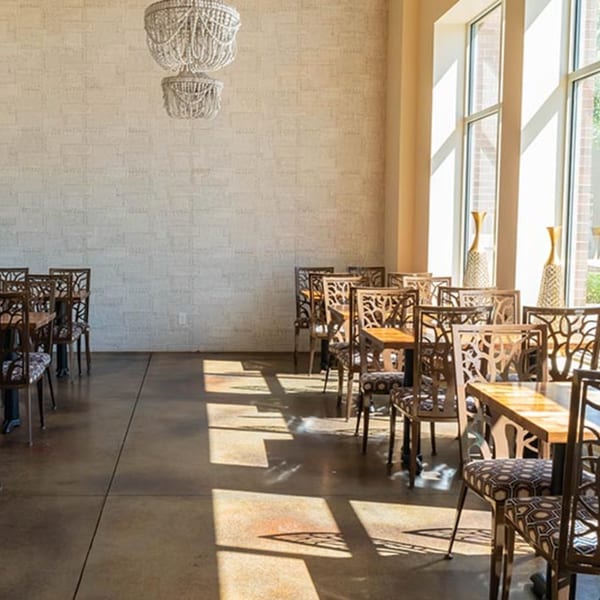 Sunlit dining room at Prados Modern Mexican Cantina with ornate chairs, wooden tables, and chandeliers.