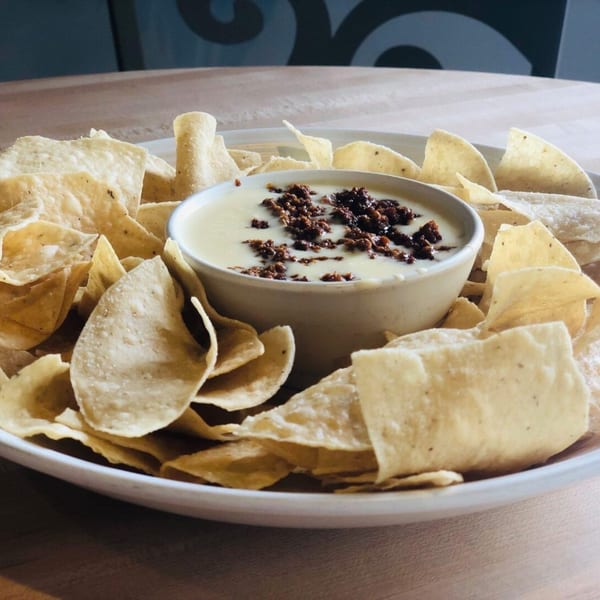 A bowl of creamy queso with ground beef, surrounded by a generous serving of tortilla chips.