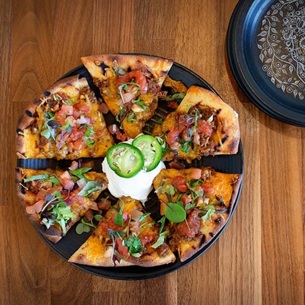 Mexican pizza cut into slices, topped with cheese, ground beef, tomatoes, and jalapeños.