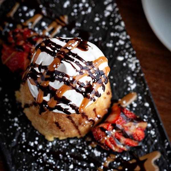 Fried ice cream dessert with whipped cream, chocolate, caramel, and strawberries on a dark plate.