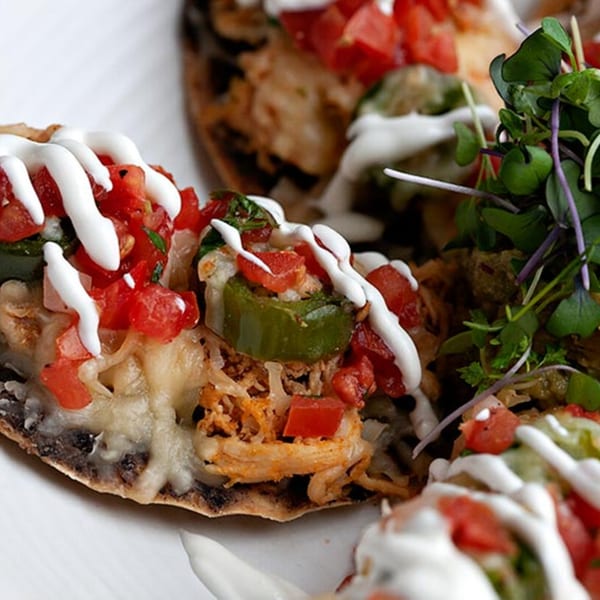 Close-up of Prados Modern Mexican Cantina's chicken tostada with melted cheese, pico de gallo, jalapeños, and crema.