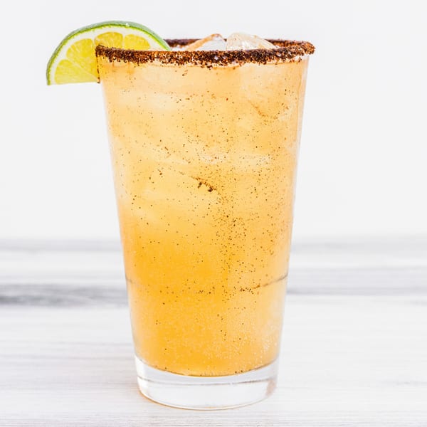 A Prados Mexican Cantina drink with a chili-lime rim and a lime wedge garnish.