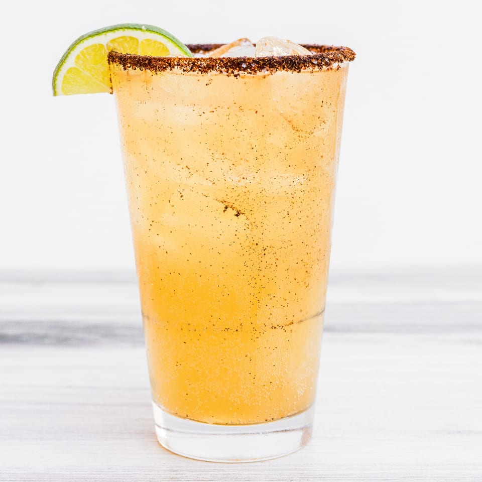 A Prados Mexican Cantina drink with a chili-lime rim and a lime wedge garnish.