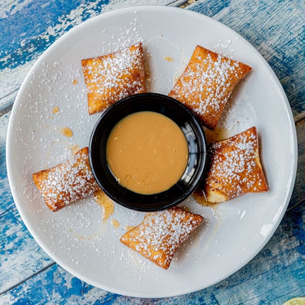 Five Prados Mexican Cantina churro bites dusted with powdered sugar, surrounding a bowl of caramel sauce.