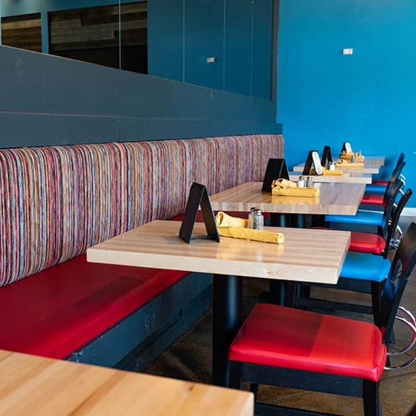 Interior of Prados Modern Mexican Cantina with colorful striped booth seating, light wood tables, and blue walls.
