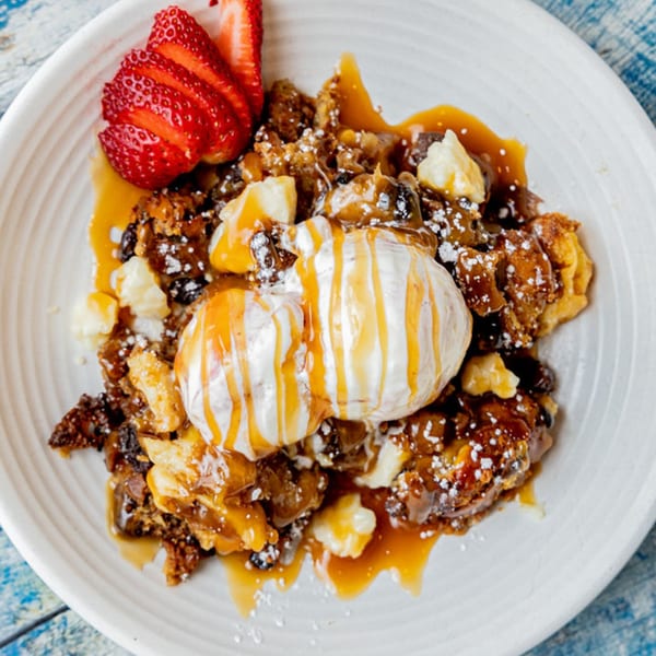 Mexican bread pudding dessert with ice cream, caramel, powdered sugar, and sliced strawberries.