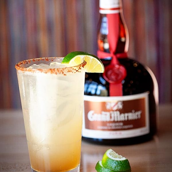 A Prados Modern Mexican Cantina margarita with a chili-lime rim and lime wedge, with a Grand Marnier bottle.