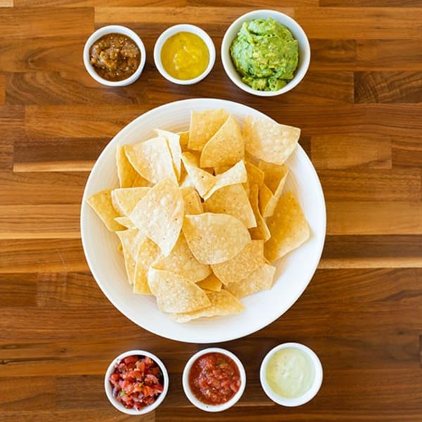 Prados Modern Mexican Cantina's tortilla chips with guacamole, salsa, and other dips on a wooden table.
