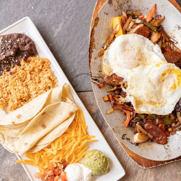 Mexican fajitas with chorizo, peppers, onions, fried eggs, rice, beans, tortillas, cheese, pico de gallo, and guacamole.