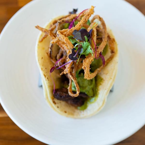 A Prados Modern Mexican Cantina taco with crispy fried onions, green sauce, and dark meat.