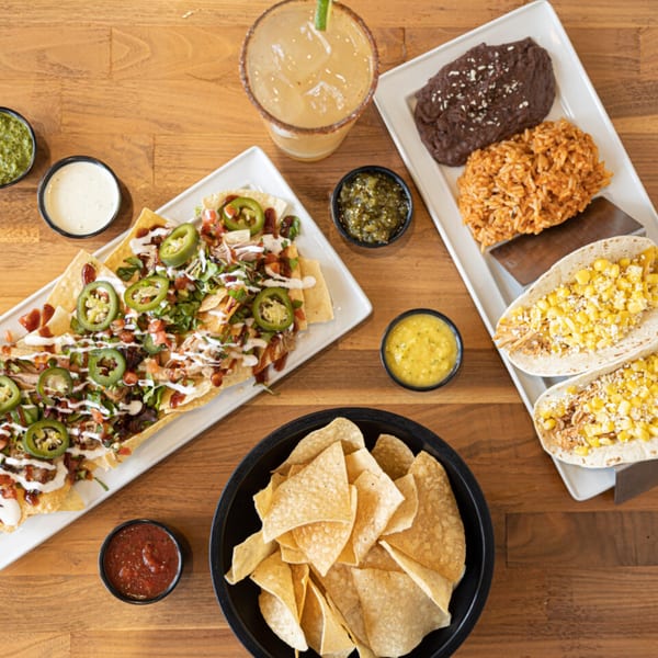 Overhead view of Prados Modern Mexican Cantina's nachos, tacos, rice, beans, chips, salsa, and margarita.