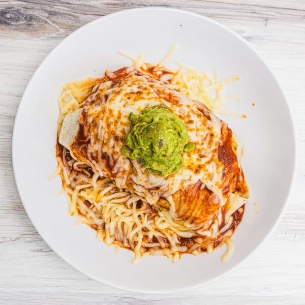 Prados Modern Mexican Cantina's cheesy burrito covered in red sauce and guacamole on a white plate.