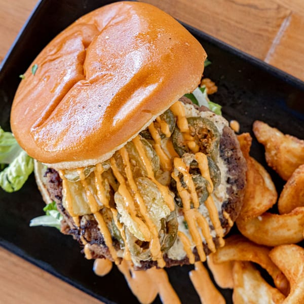 Prados Modern Mexican Cantina's burger with jalapeños, sauce, and a side of potato wedges.