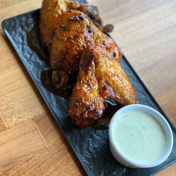 Prados Modern Mexican Cantina's glazed chicken wings with a side of creamy dipping sauce on a black plate.
