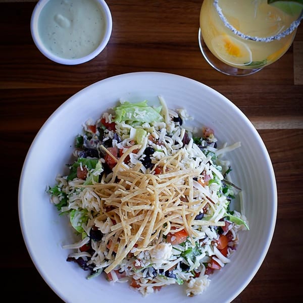Overhead view of a Prados Modern Mexican Cantina salad with dressing and a margarita.