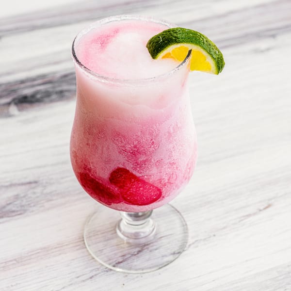 A frosty pink Prados Modern Mexican Cantina margarita with a lime wedge and red fruit on a white table.