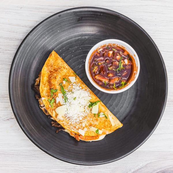 A Prados Modern Mexican Cantina quesadilla with cheese and herbs, served with a side of dipping sauce.