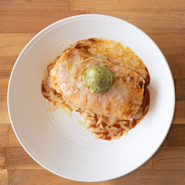 Prados Modern Mexican Cantina's enchilada dish with a dollop of guacamole on a white plate.