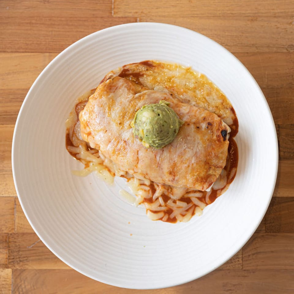 Prados Modern Mexican Cantina's enchilada dish with a dollop of guacamole on a white plate.