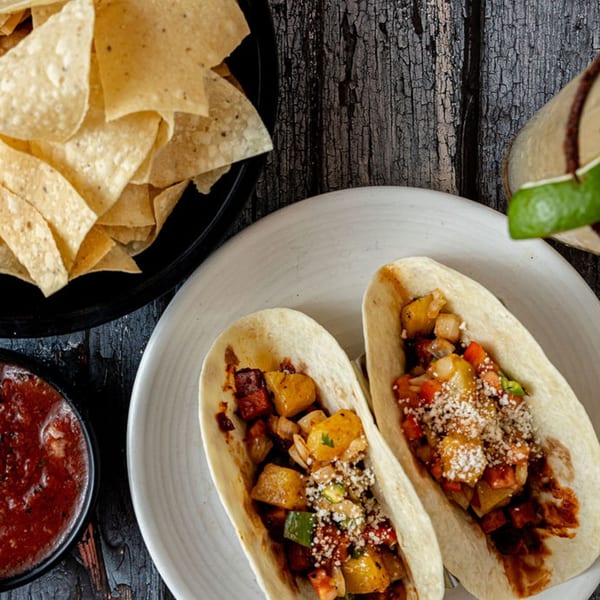 Two Prados Modern Mexican Cantina tacos with chips, salsa, and a drink on a dark wooden table.