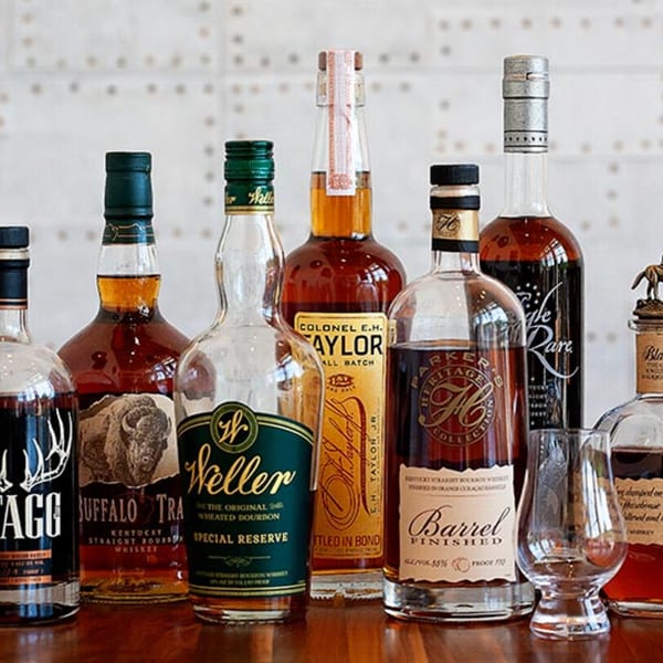 A collection of various bourbon and whiskey bottles, including Buffalo Trace and Weller, on a wooden surface.