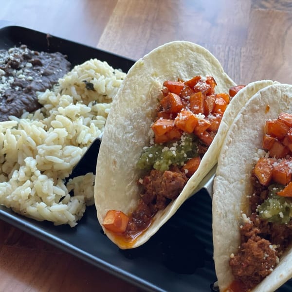 Two Prados Modern Mexican Cantina tacos with rice and black beans on a black plate.