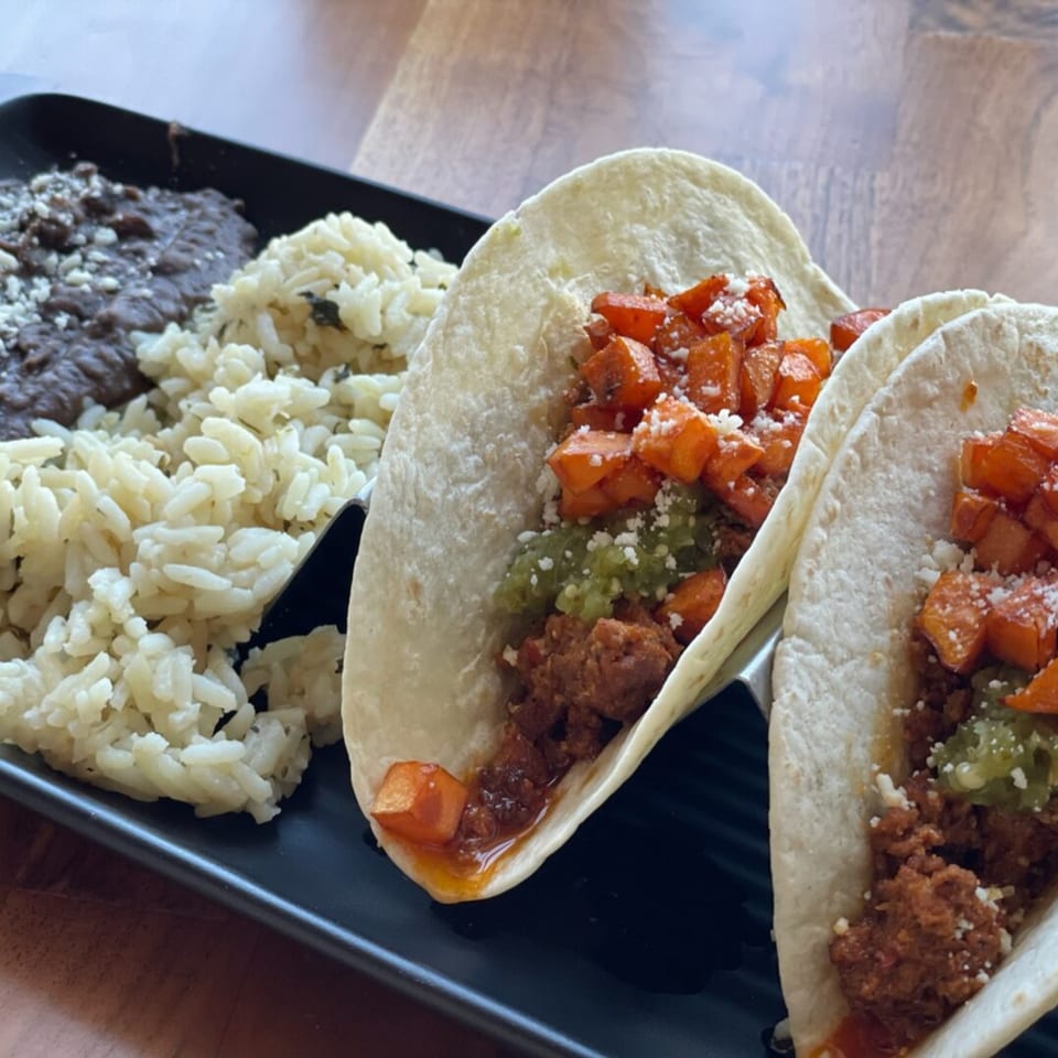 Two Prados Modern Mexican Cantina tacos with rice and black beans on a black plate.