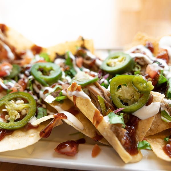 Close-up of Prados Modern Mexican Cantina's nachos with pulled pork, jalapeños, sour cream, and BBQ sauce.