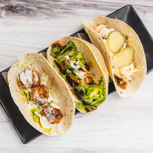 Three Prados Modern Mexican Cantina tacos with various fillings, sauces, and toppings on a black plate.