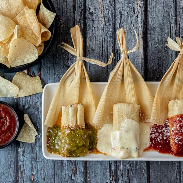 Three Prados tamales with green, white, and red sauces, alongside tortilla chips and salsa.